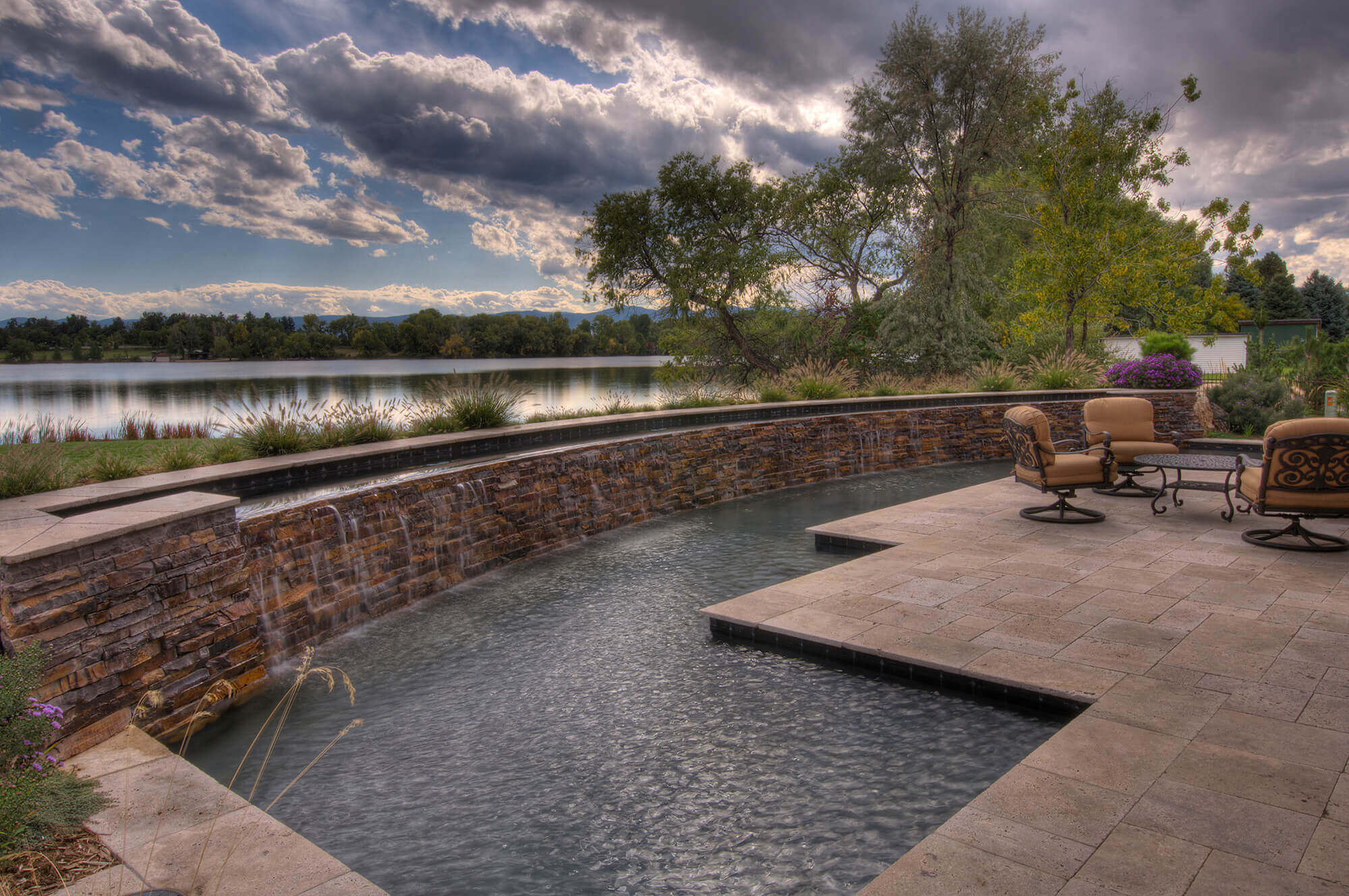 Backyard area with some chairs, tables, swimming pool and a beautiful view of the sky