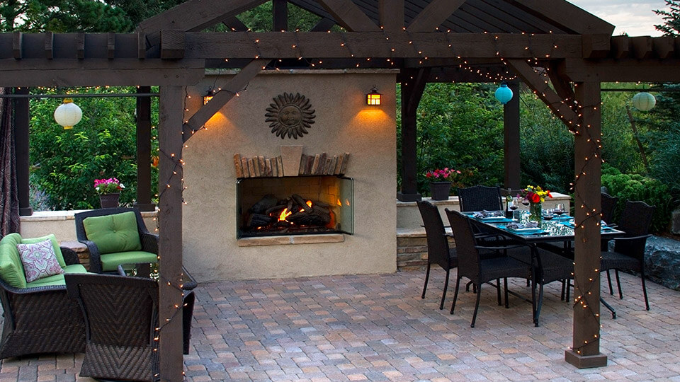 Wooden pergola with lighting, fire pit, chairs and dining setup in the backyard