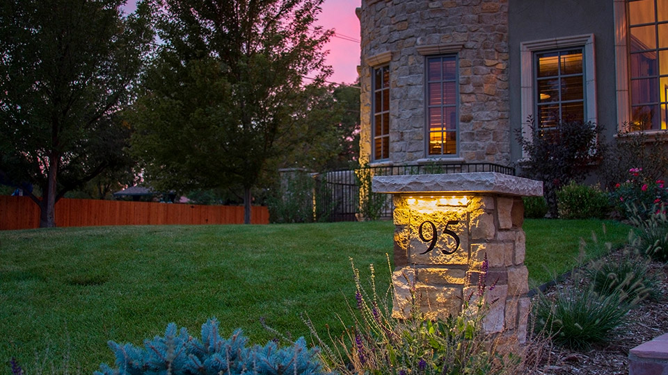 An exterior stone light post with house address number in front of the house