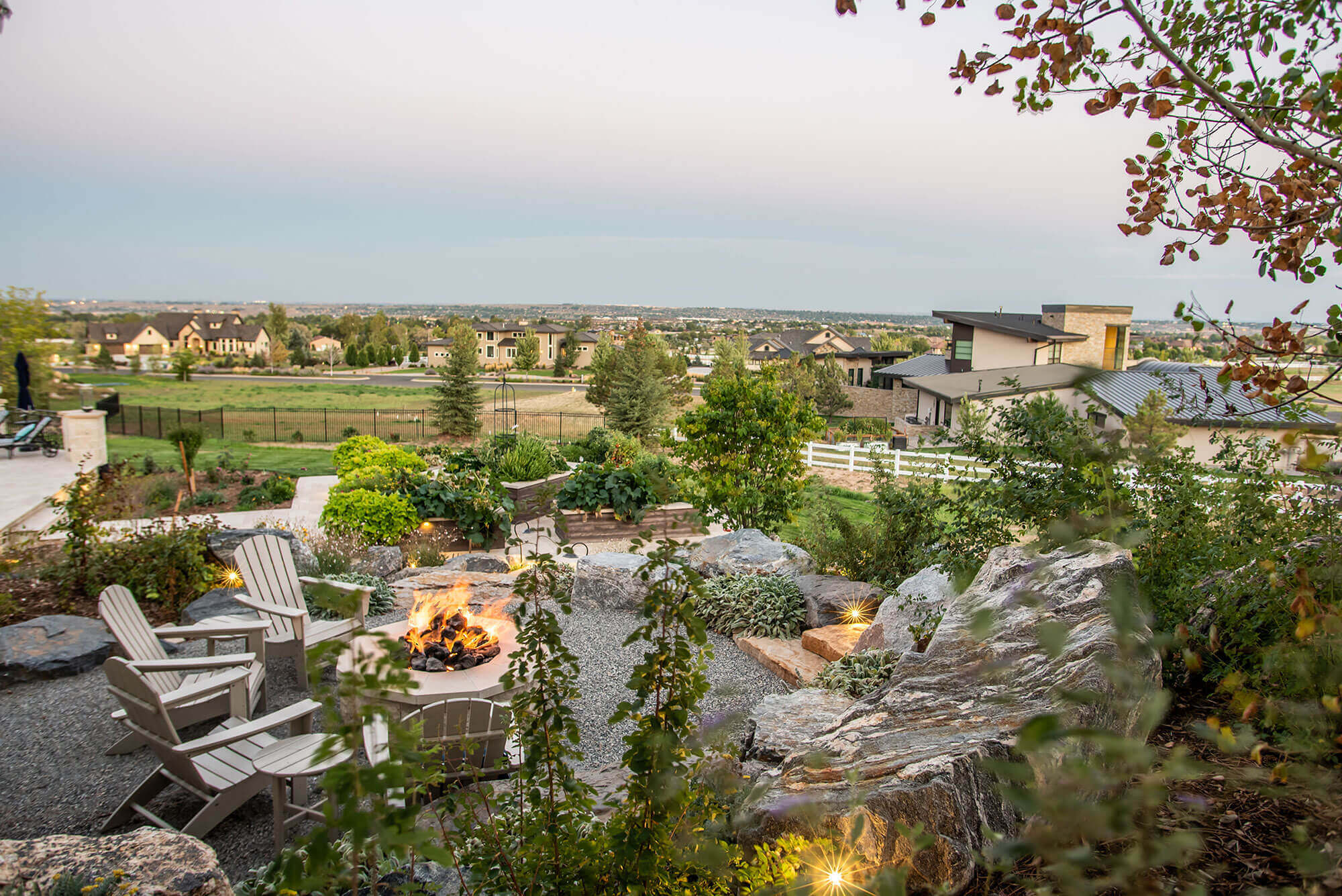 Fire pit area filled with rocks with some chairs, fire pit, plants and trees