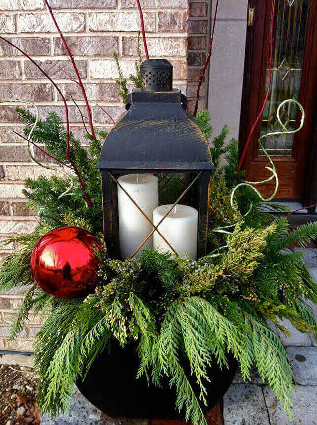 A plant is decorated with christmas bulbs, and candles in front of the house