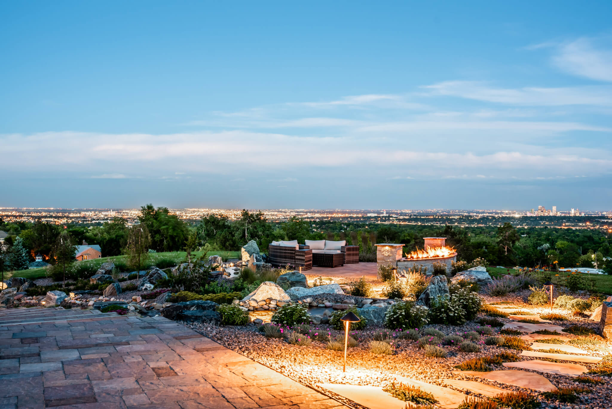 View from outdoor garden, natural gas fire pit along with sofas, flower plants, and trees