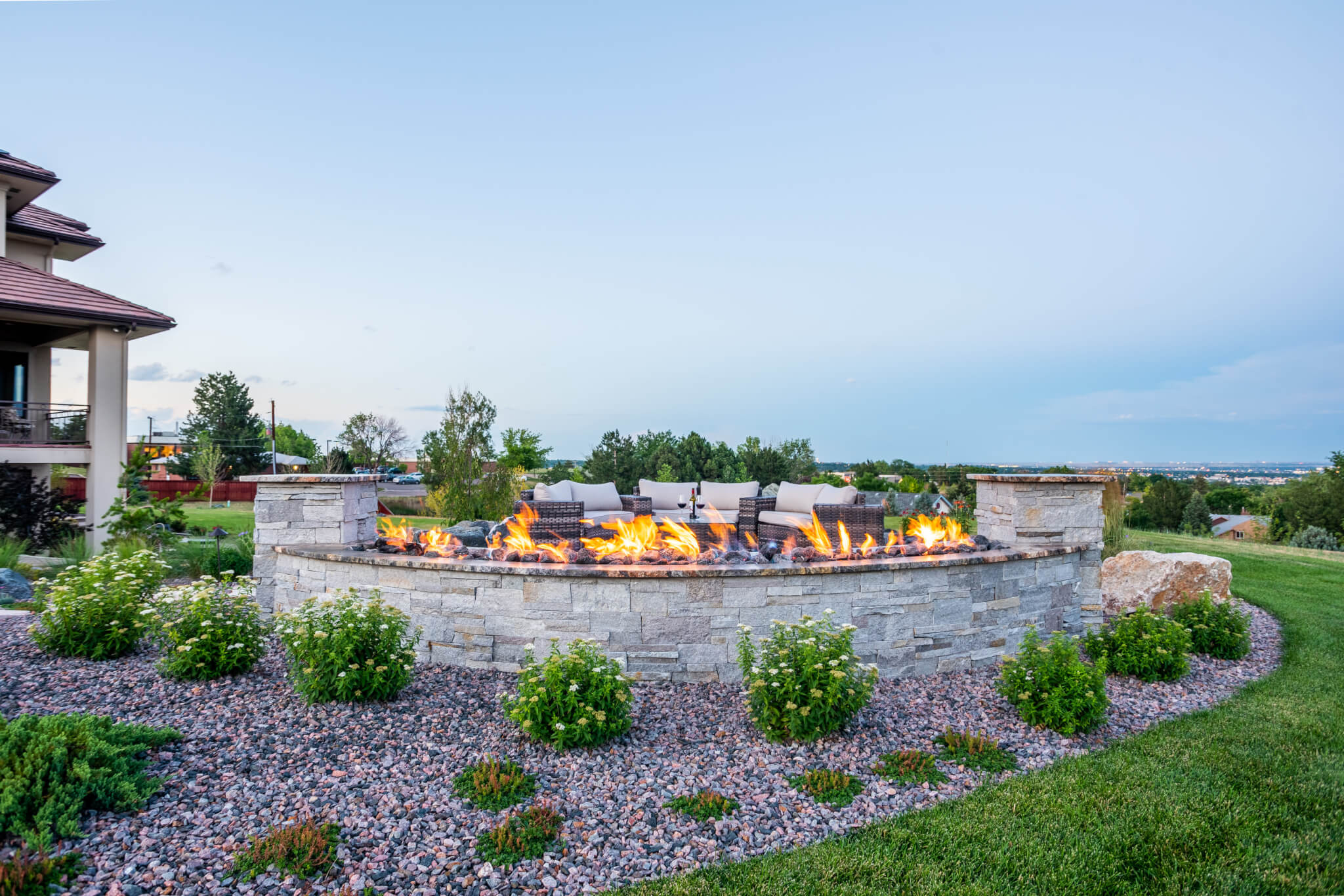 Garden area with natural gas fire pit along with sofas, flower plants, and trees