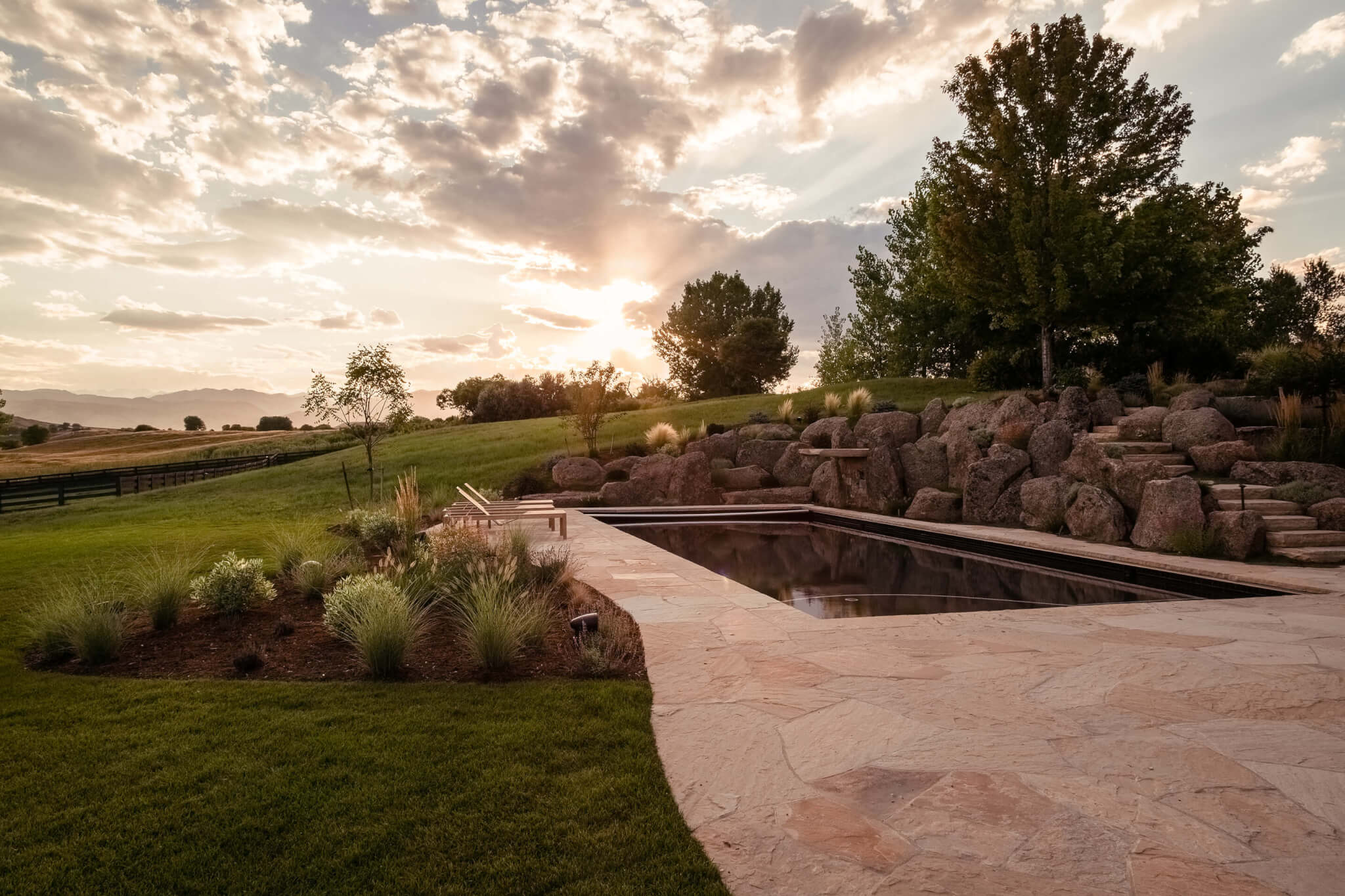 Pool area with rocks, grass plants, trees with a beautiful sky view