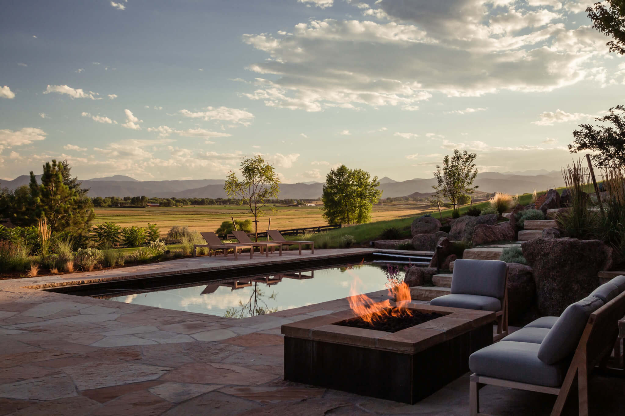 Pool area with relaxing chairs, fire pit surrounded by chairs and sofa along with sky view