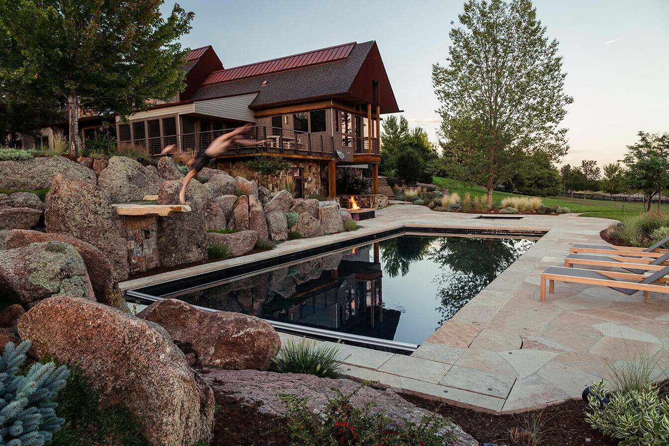 A man is jumping into the pool in the backyard