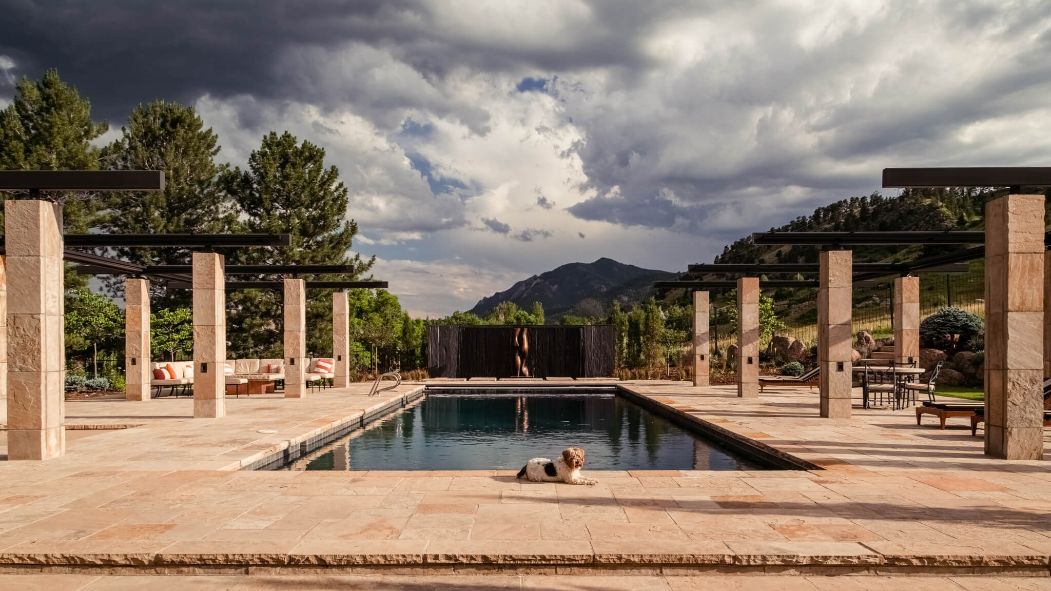 Pool area filled with sofas, resting chairs, dining chairs, table and a dog laying on the floor