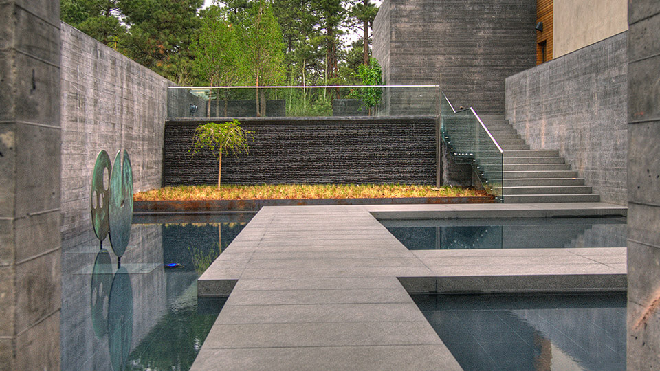 Minimalist landscape design. Concrete walkway with natural concrete walls with a dripping wall fountain in the background