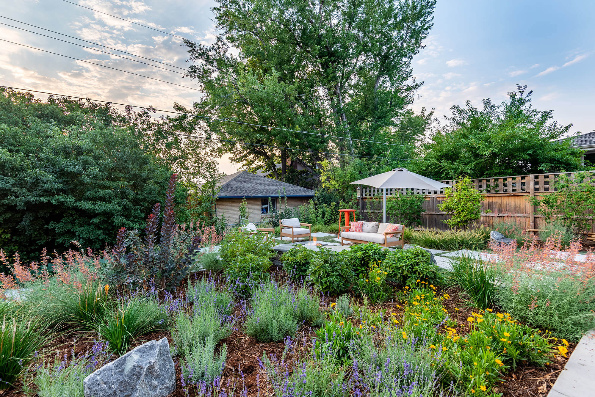 Lawn area with plants, trees, table, chairs, sofa around fire pit