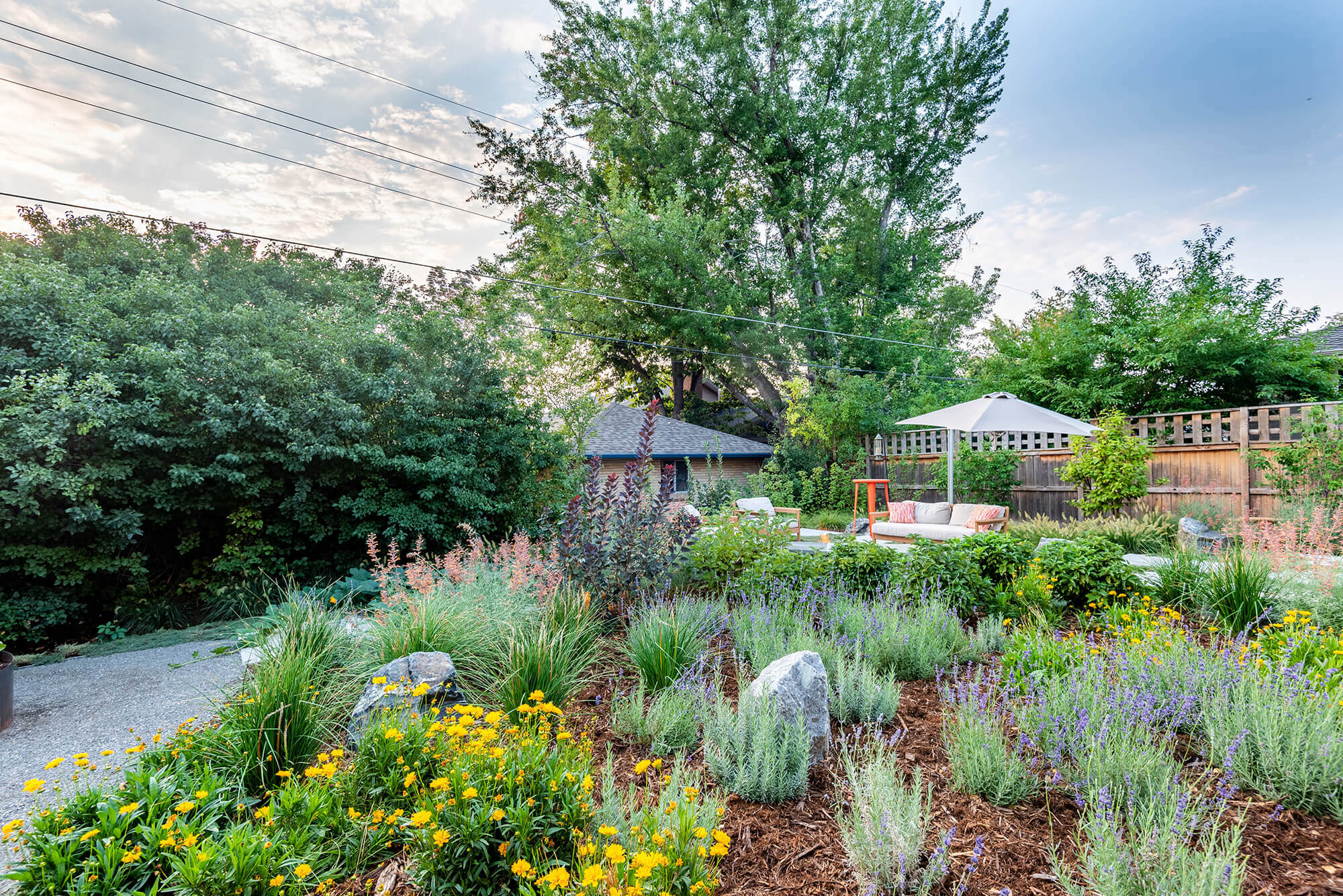 Garden area with plants, trees, table, chairs, sofa around fire pit