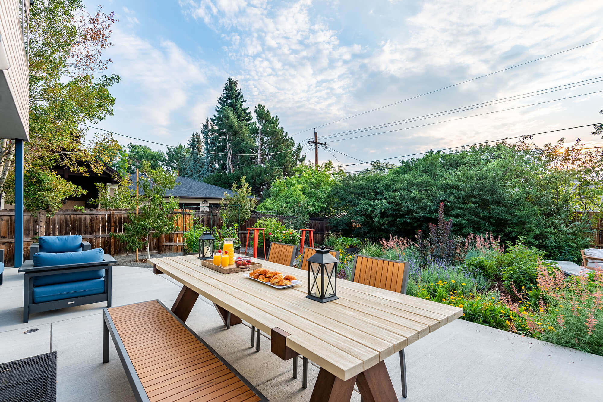 Outside dining table with some fruits, snacks, Juice and candle holders on it in the garden area