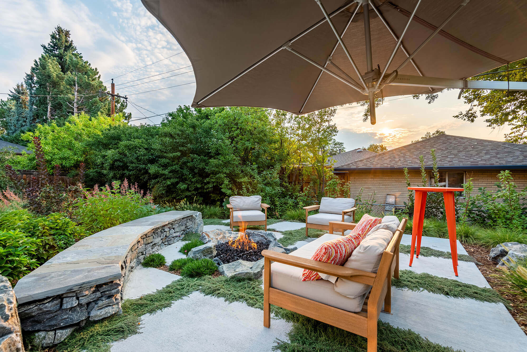 Lawn area filled with rocks, sitting table, chairs, plants, trees, and fire pit