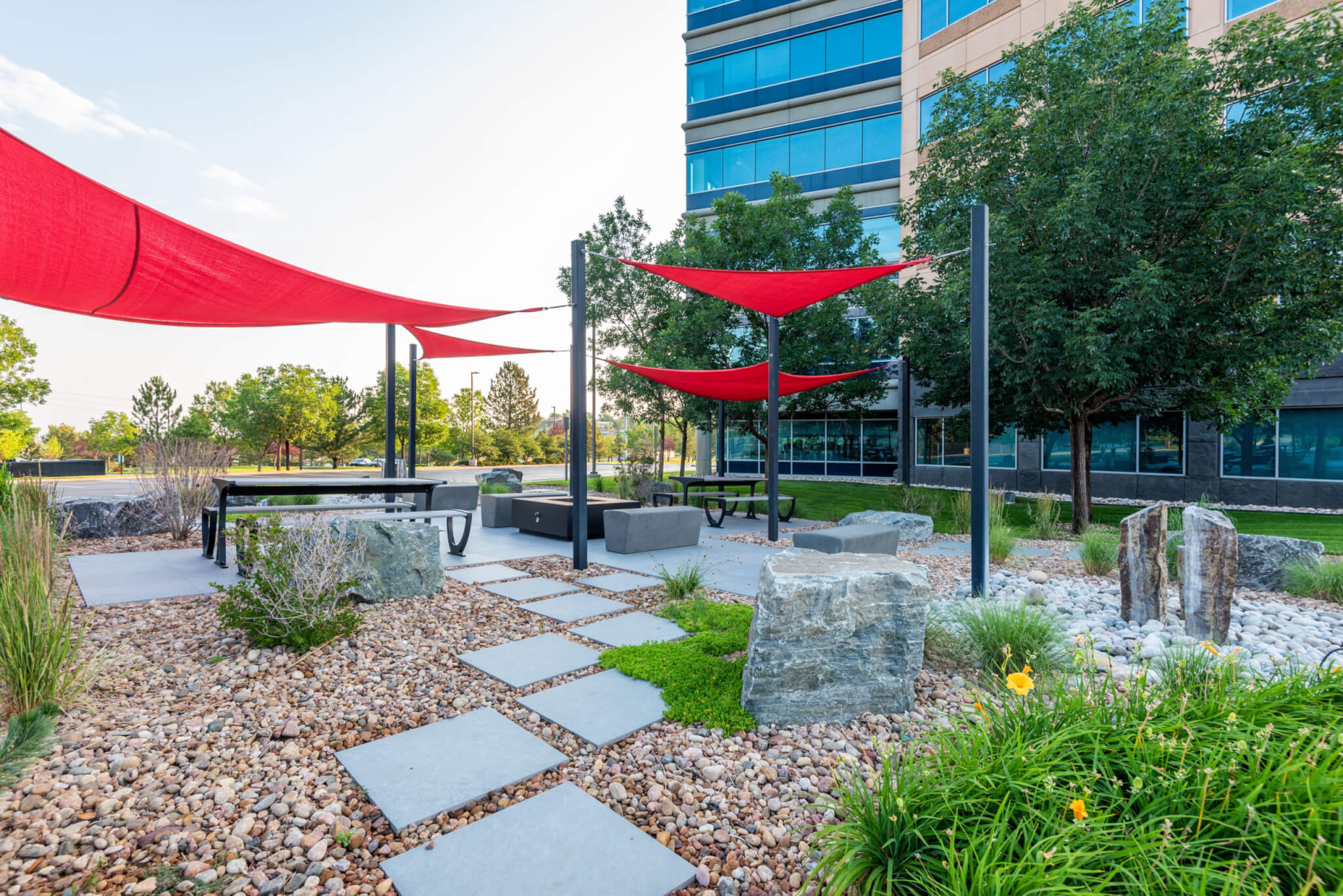 Sitting benches with red fabric tensile membrane with sail shade structure in front of the tinted glass building