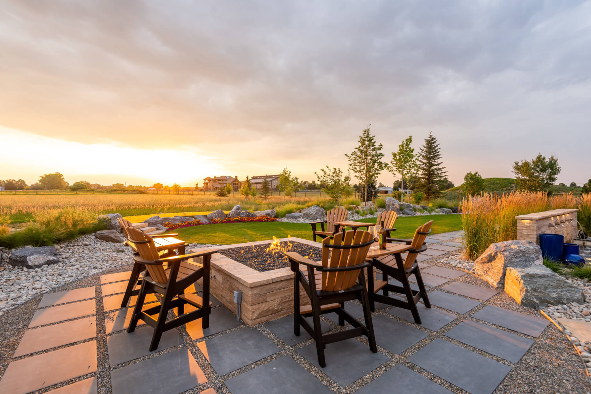 Sitting area along with chairs around the fire pit, colored flower plants, tress and landscape view