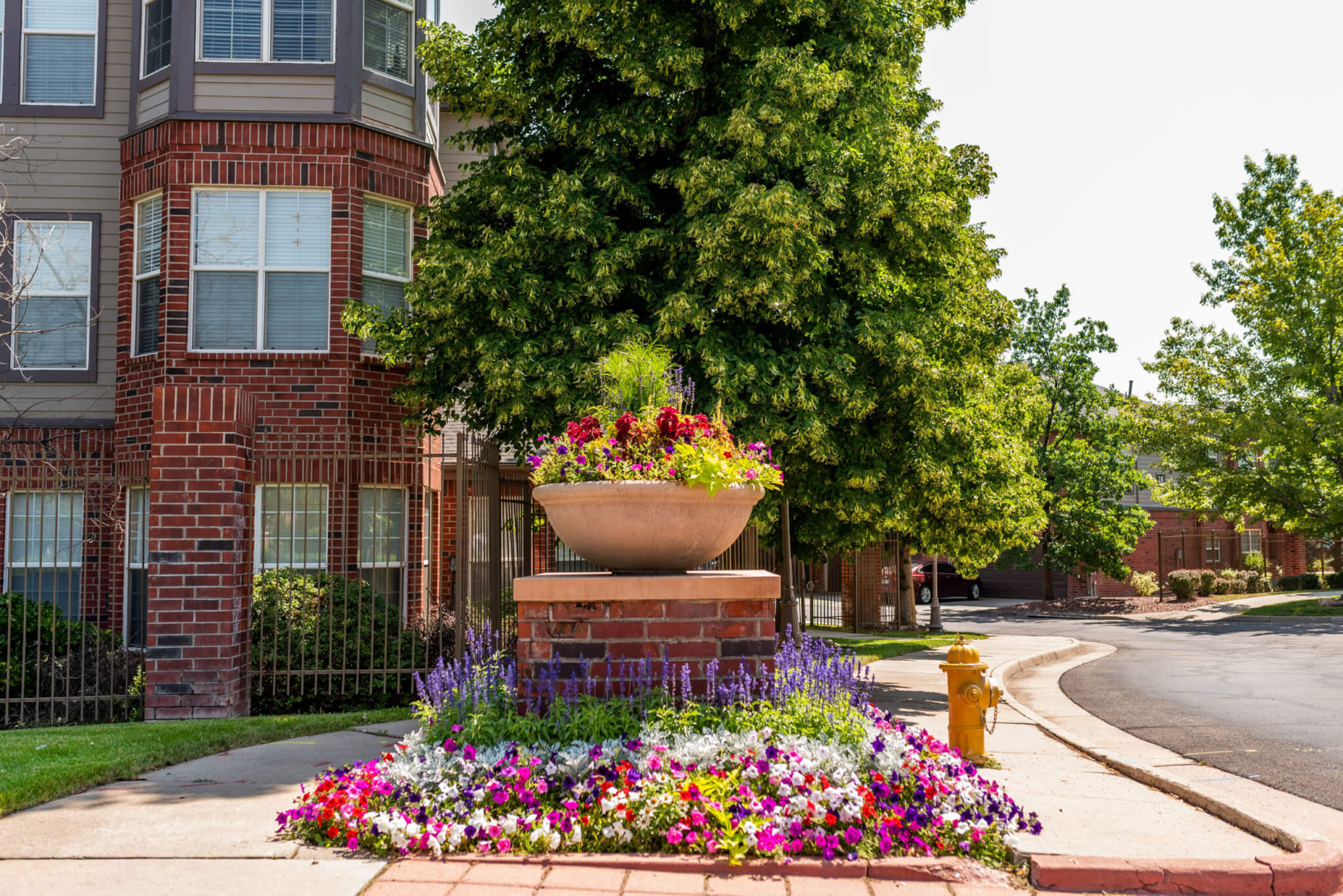 A building with a big flower pot filled with plants and colourful flower plats in front of it