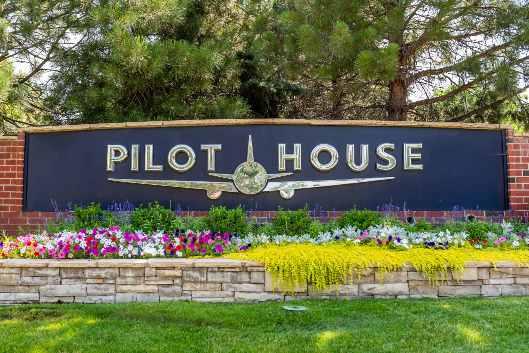 A big stacked stone flower pot is filled with creeper plants and colour flower plants in front of the pilot house sign