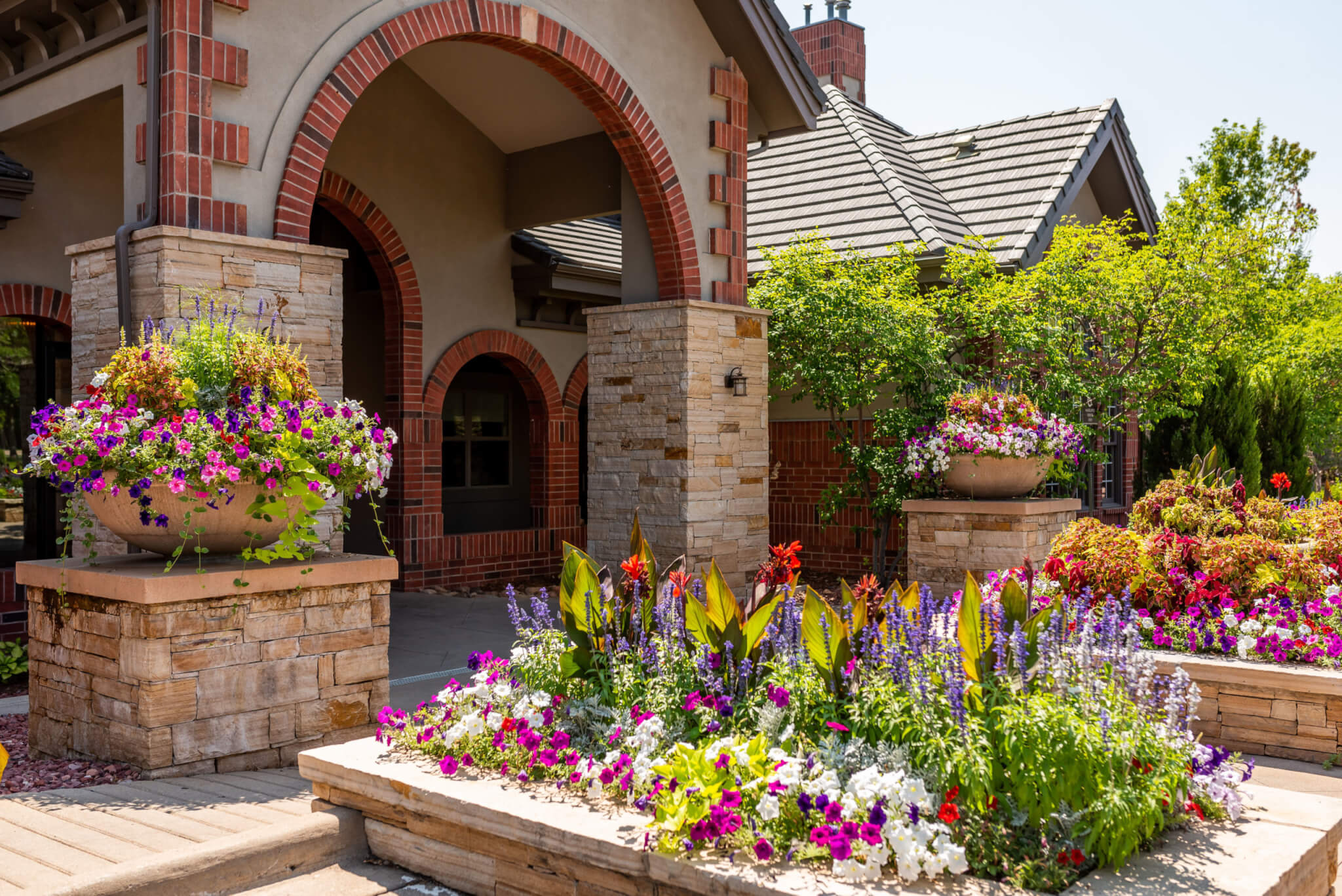 Stacked stone flower pots, big clay flower pots are filled with different types of plants and colourful flower plants in front of a building