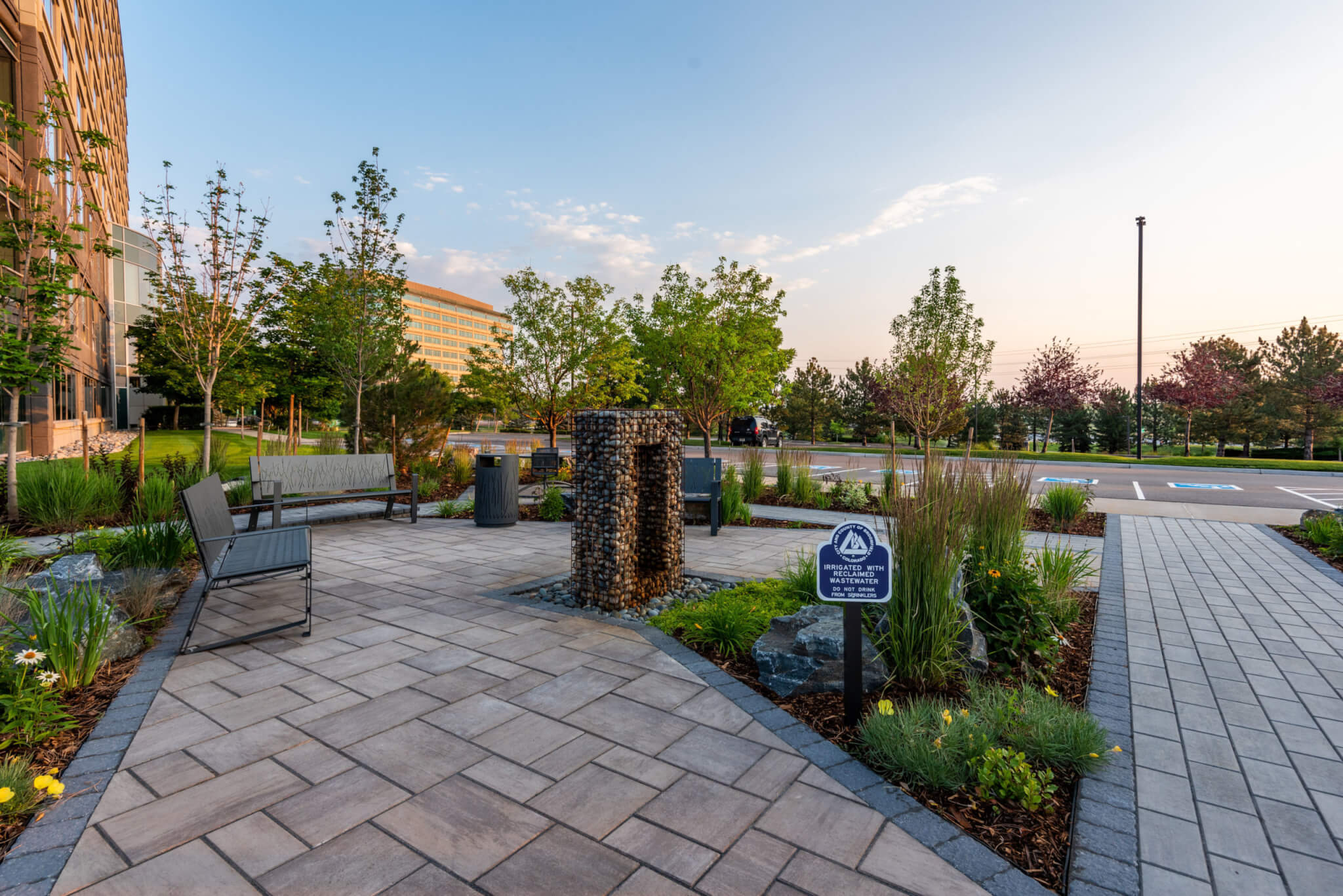 Sitting area with metal benches along with a metal cage filled with rocks, plants and trees outside of the building