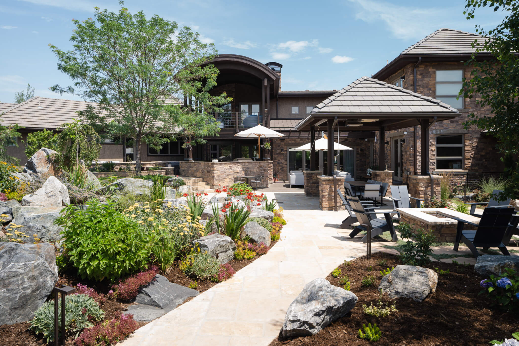 View of a backyard showing gazebo, firepit, chairs plants, and a pathway