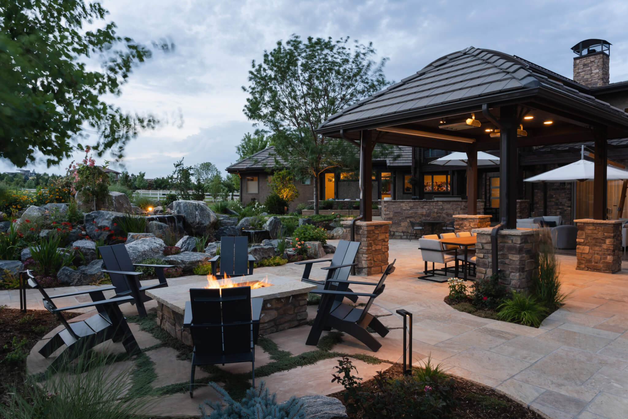 Man-made constructed mini water fall, chairs around fire pit, and out door dining in the backyard