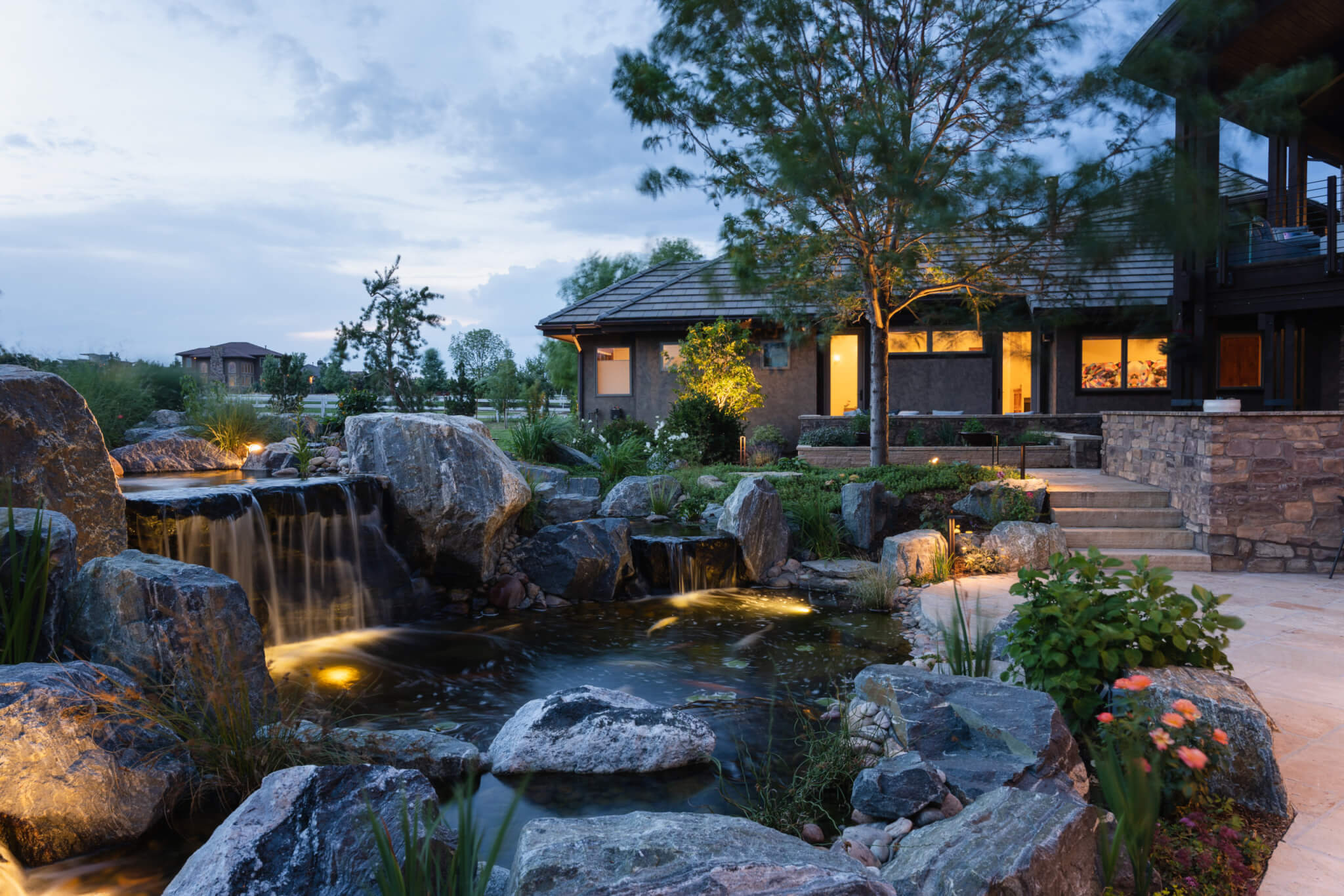 Koi fish pond with a man-made constructed mini waterfall with plants and trees in the backyard