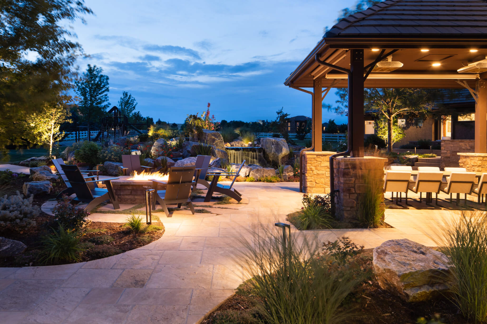 Man-made constructed mini water fall, chairs around fire pit, and out door dining in the backyard