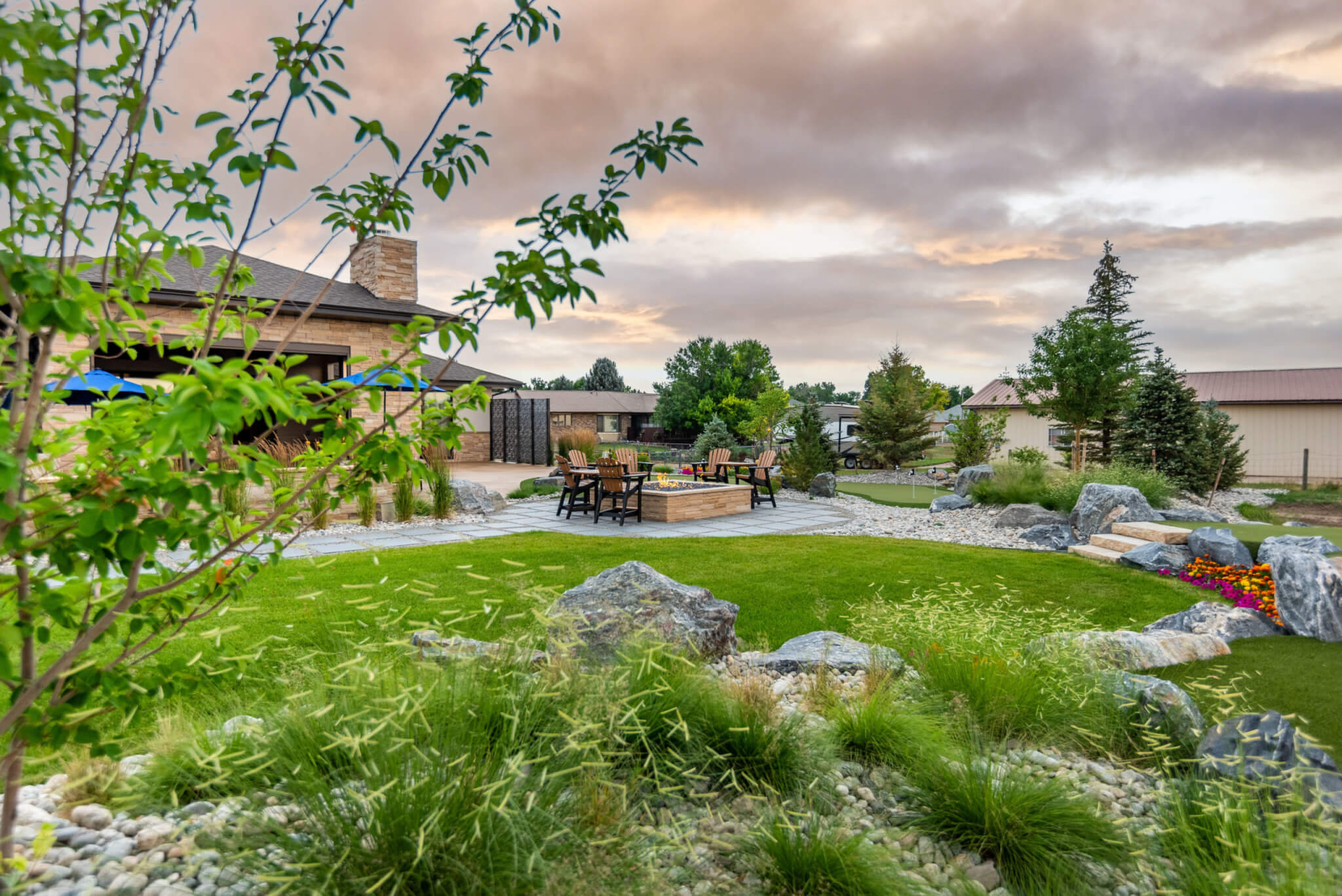 Backyard area along with chairs around the fire pit, colored flower plants, tress and a beautiful sky view