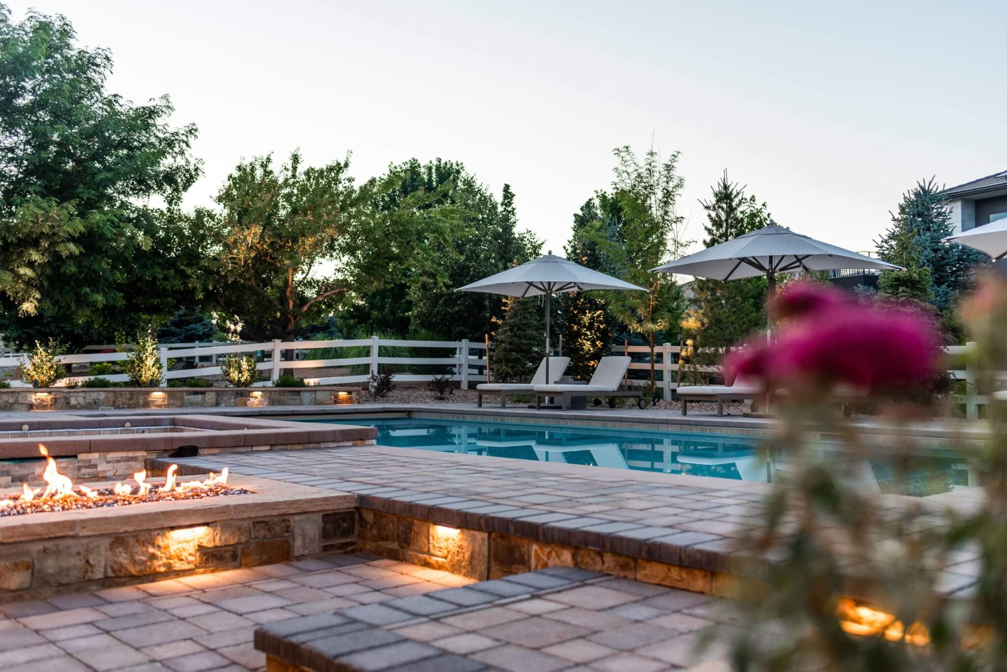 Swimming pool area with fire pit along with chairs, umbrellas, plants, and trees