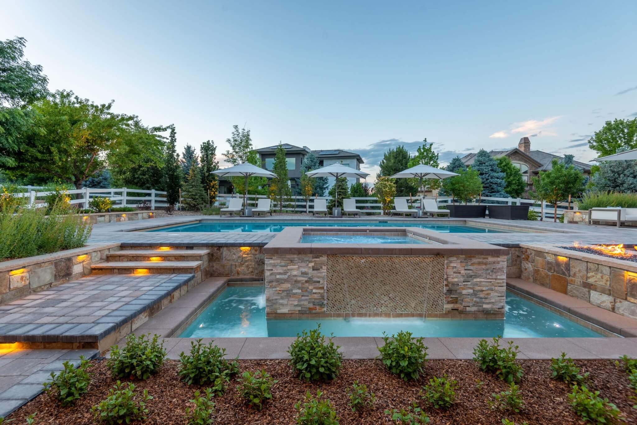 Swimming pool area with fire pit along with chairs, umbrellas, plants, and trees