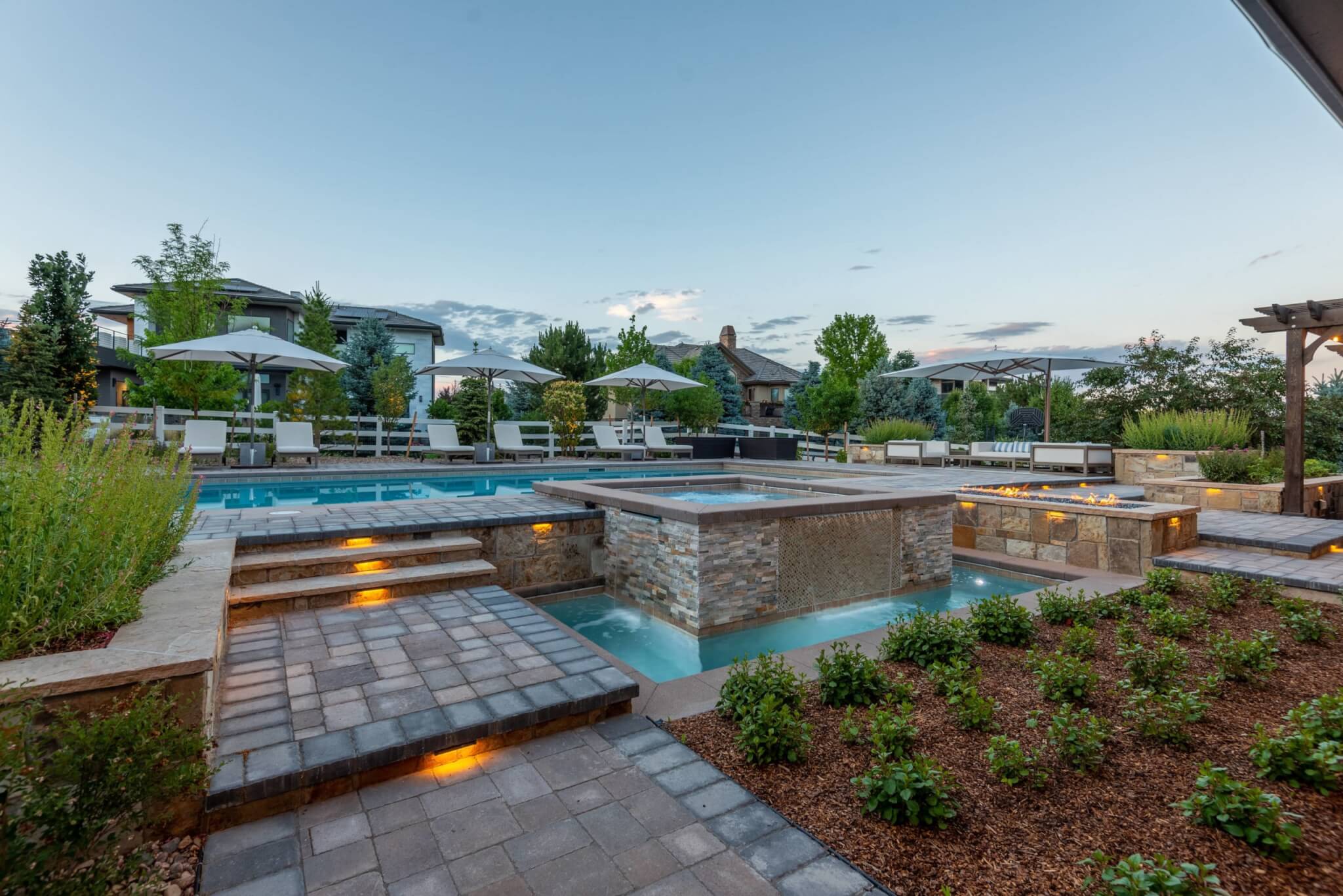 Pathway to swimming pool area with fire pit along with chairs, umbrellas, plants, and trees