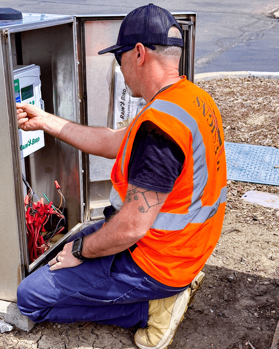 Environmental Designs Worker crouched working on a Smart Irrigation System with an orange vest in the sun