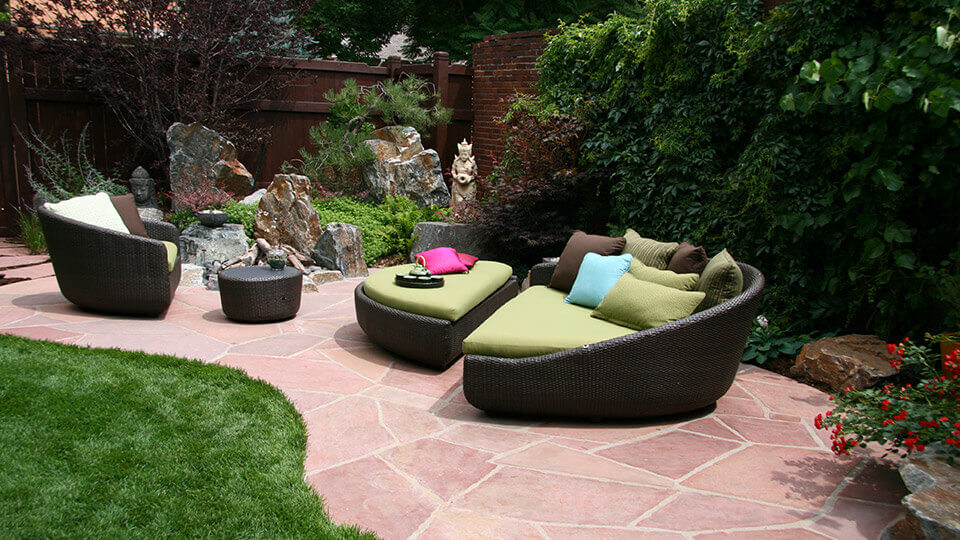 backyard with stone pavers and modern round green white and black patio furniture. boulders and fountain feature in the background