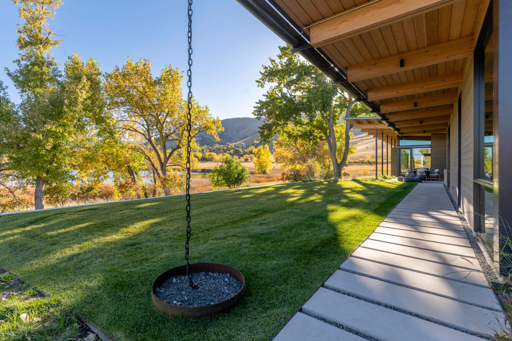 Outside of a house with a pathway that is surrounded with a lawn, plants, trees, and chain hanging from the ceiling